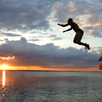 Boy jumping off a dock at sunset