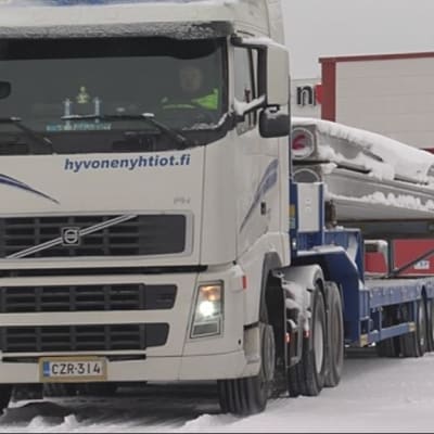 Rekka-auto lähdössä tehtaan pihalta betonipalkkilastissa