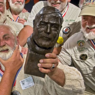 Ernest Hemingway yhdennäköisyyskilpailun osanottajia. Voittaja kannattelee Hemingwayn veistosta käsissään.