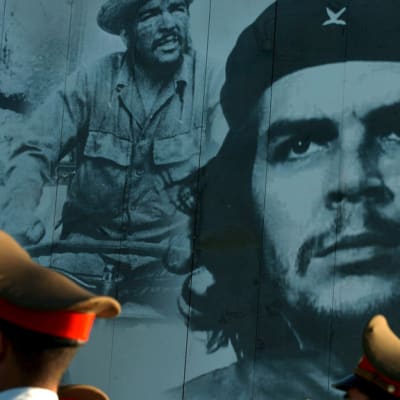 Suuri valokuva Chestä, edessä ohi marssivien sotilaiden lakkeja.
