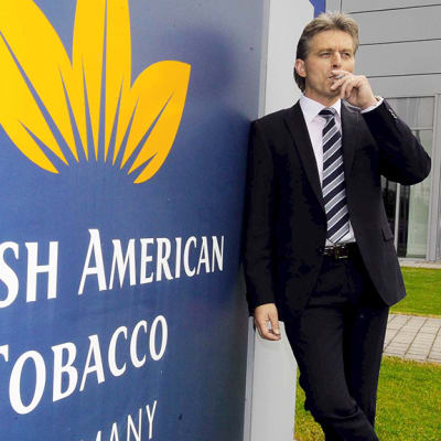 Mies tupakoi British american Tobaccon kyltin vieressä.