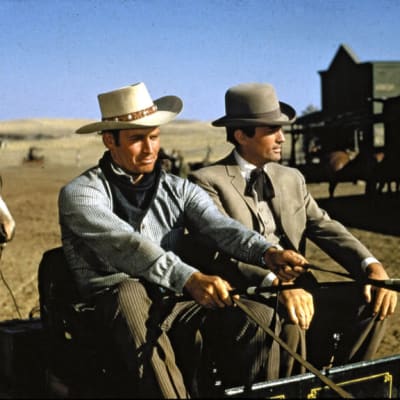 Kaksi miestä (Charlton Heston ja Gregory Peck) istuvat pienessä hevoskärryssä ajaen lännenkaupungin kadulla.