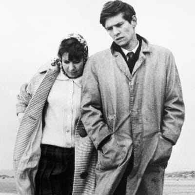 Nuori mies (Tom Courtenay) ja nainen kävelevät merenrannalla.