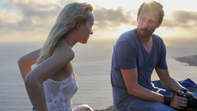 Dakota Johnson och Matthias Schoenaerts utbyter blickar sittande på en mur på italiensk ö.