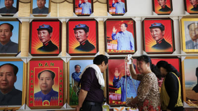 Besökare tittar på souvenirer framför en vägg med porträtt av Mao Zedong i Shaoshan i Hunanprovinsen i Kina. Shaoshan var Maos hemstad.