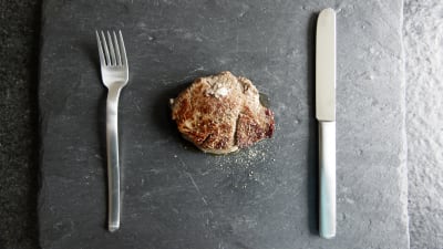 Bild på en biff på ett fat med kniv och gaffel på sidan om.