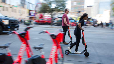 En man och en kvinna i Austin i Texas åker sparkcykel i riktning högerut på bilden. 