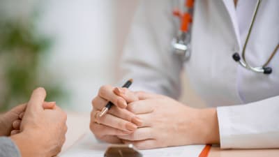 Närbild av händerna av en läkare och dennes patient. De sitter mot varandra och samtalar.