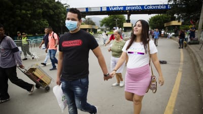 Ett par går hand i hand på gatan. Han har munskydd och hon är gravid i rosa kjol.