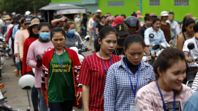 Kvinnor står i en kö utanför en fabrik i Kambodja. De är klädda i färggranna kläder.