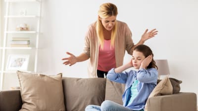 en mamma grälar med sin dotter som sitter på soffan och håller för öronen