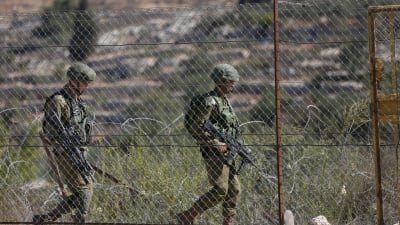 Två israeliska soldater går bakom hönsnät. 
