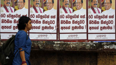 En kvinna går förbi en vägg täckt av planscher på president Sirisena och nya premiärministern Rajapaksa 