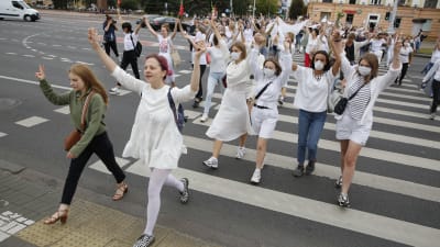 Eb grupp vitklädda marscherar över en gata med uppsträckta händer