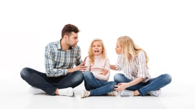 en mamma och pappa sitter på golvet och försöker diskutera med sin dotter som gråter