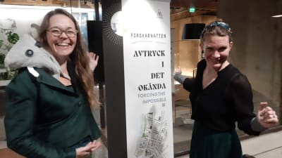 Laura Hellsten och Minna Aalto sätter upp en vit banderoll för Forskarnatten - Avtryck i det okända.