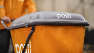 En orange postvagn med texten "Posti" på skuffas av en orangeklädd brevbärare.