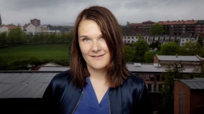 Porträttbild av Marie Aubert som tittar rakt in i kameran med höghus och en park i bakgrunden. 