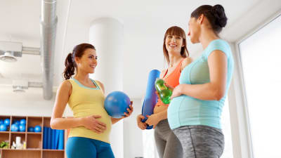 Tre gravidakvinnor i träningskläder ler mot varandra