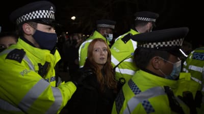 En kvinna omgiven av flera poliser. En av poliserna håller i kvinnans arm. Poliserna har munskydd.