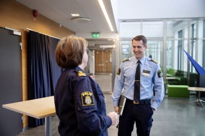 Två poliser i uniform, en kvinna och en man, pratar med varandra i kontorsliknande lokal.