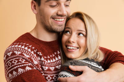 Man och kvinna i liknande stickade tröjor kramar om varandra och ler