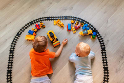 Två barn sitter och tecknar på golvet, omringade av leksaker.