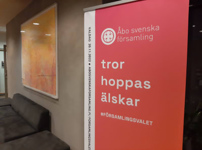 En röd, hög affisch med texten Åbo svenska församling, tro hoppas älskar och #församlingsvalet.