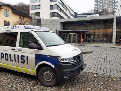 En polisbil står parkerad på en stenlagd innergård vid ett hus med glasväggar. Ovanför ingången finns texten Turun oikeustalo Åbo rättscenter.