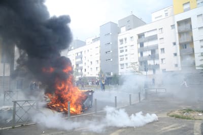 Sopkärl brinner på en gata mellan förortshus i Frankrike.