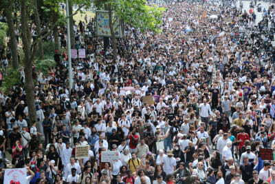 En folkmassa vandrar fram längs en gata. Många är klädda i vita t-tröjor och skjortor.
