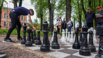 En ung man flyttar på en stor schackpjäs i en park.