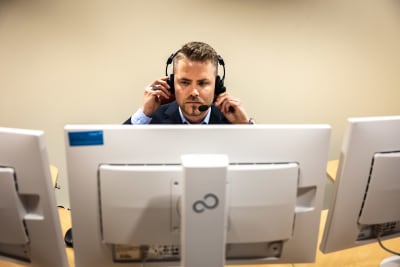 Man i kavaj och hörlurar sitter bakom datornskärmar