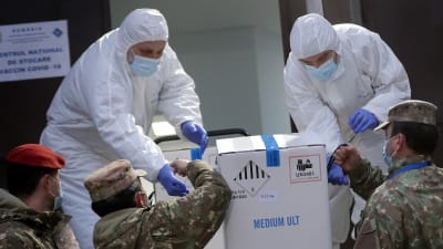 Soldater lyfter upp en låda med coronavaccin åt två personer i skyddsutrustning som tar emot lådan.