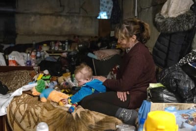 Kvinna med litet barn på en säng i ett bombskydd i Ukraina. 
