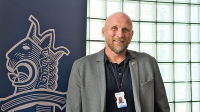 En kavajklädd man står intill polisens blåa banderoll med polisens vapen på.