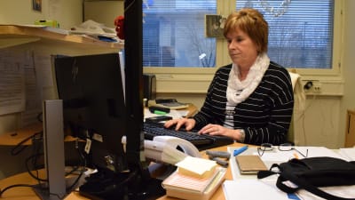 Ann-Marie Kinos sitter vid sitt arbetsbord framför datorn.