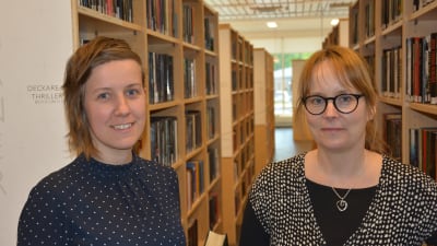 Jolanda Raitio och Karolina Zilliacus står mellan böcker i ett bibliotek.