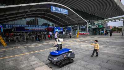 En polisrobot påminner människor om att de ska bära skyddsmask, och mäter febern på dem.  Shenzhen,  provinsen Guangdong 6.3.2020 