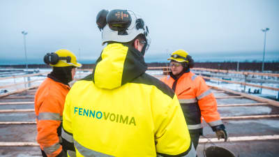 Tre män i grälla arbetskläder på Fennovoimas bygge.