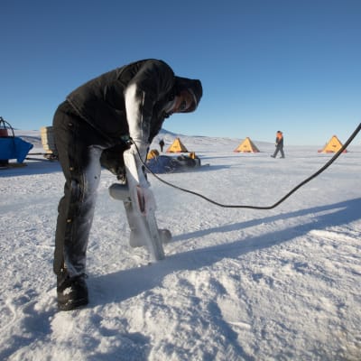 En person sågar igenom isen i Antarktis. 