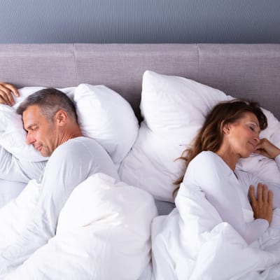 man och kvinna sover med ryggarna mot varandra, både belåtet leende