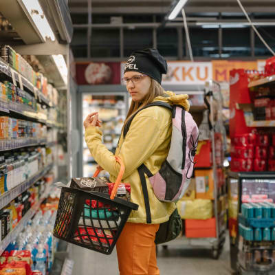 En ung kvinna tittar bekymrat på priserna i en butikshylla.