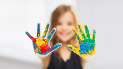 En flicka visar sina händer som är täckta av olika färgs målärger till kameran.