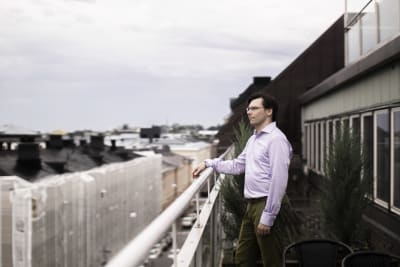 En man står på en balkong. Han ser ut över Helsingfors. 