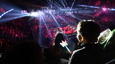En översiktsbild av en arena fylld av publik. Längst fram i arenan en scen, i förgrunden ett barn.