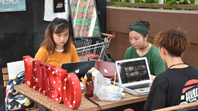 Tre studerande sitter och studerar med sina datorer vid ett bord.