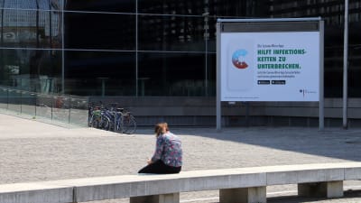 En kvinna sitter med sin mobiltelefon framför en reklam för den tyska corona-appen.