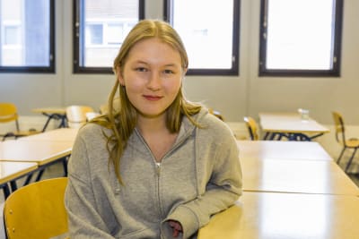 Gymnasieeleven Lila Leinonen sitter vid en pulpet i ett klassrum och ser in i kameran. 