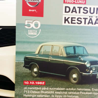 Datsun Bluebird juliste uuden Nissanin edessä.